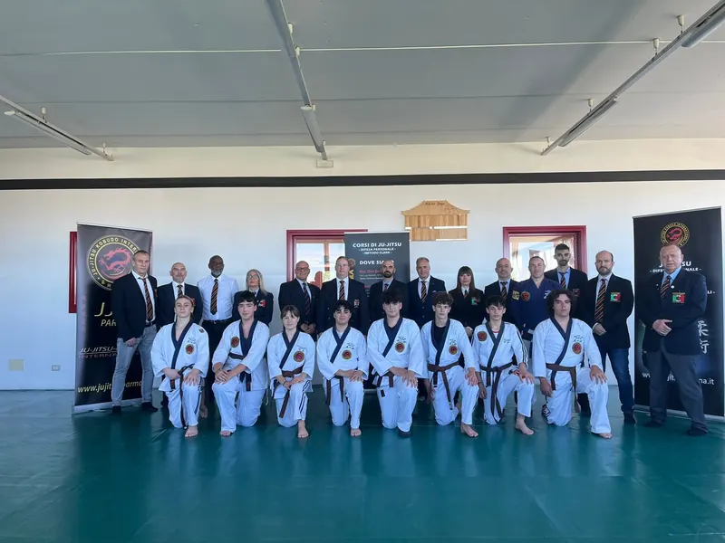Stage: allievi in divisa bianca in ginocchio sul tatami, con i maestri in giacca alle loro spalle
